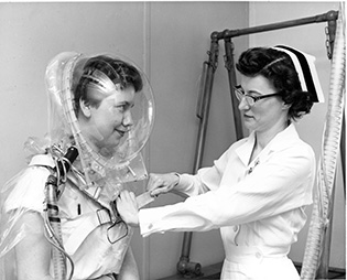Female patient wearing a clear helmet that covers her face and head; a nurse helping her