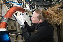  Kate Rubins looking at an orange hose aboard the International Space Station.