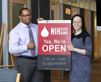 Hal Wilkins (left) and Dr. Kamille West-Mitchell (right) pose with a sign for the NIH Blood Bank