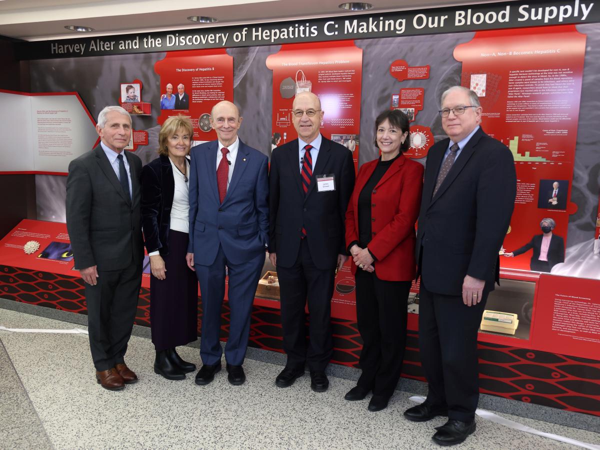 Harvey Alter with NIH leaders standing in front of a red-themed display