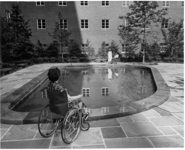 Black and white image of NIH Clinical Center reflecting pool and patient in a wheelchair