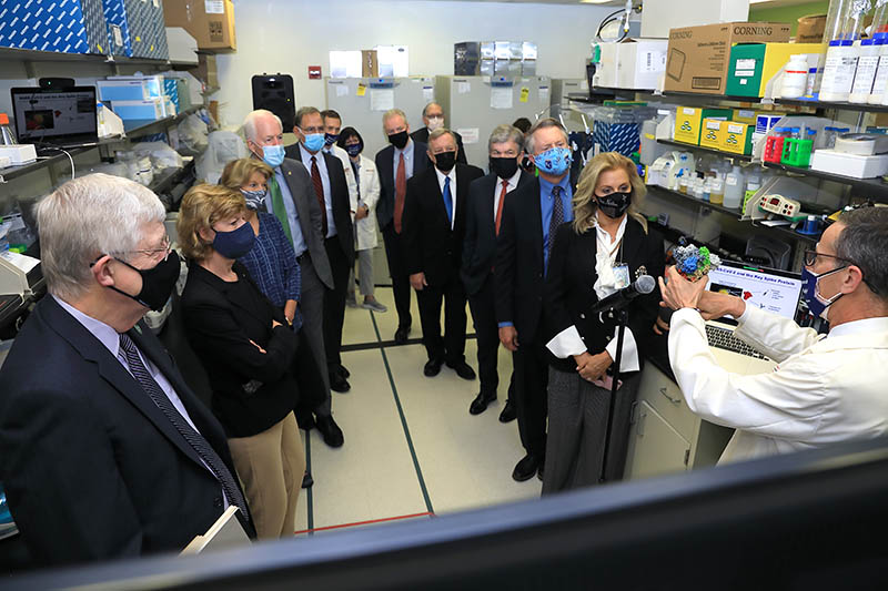 A group of people, dressed in business attire, listening to a scientist talk. 