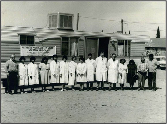 group of about a dozen people standing outside a small clinic building