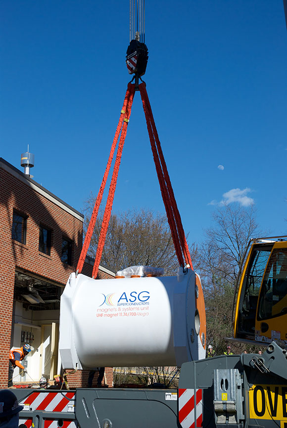 Giant MRI magnet being held by straps hanging from a crane