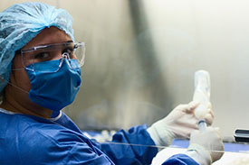 Woman wearing medical protective gear--hair covering, mask, gloves, and jacket.