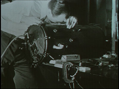 screen capture from film showing scientist peering into a decompression chamber