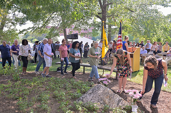 people lined up outside and putting flowers on a plaque