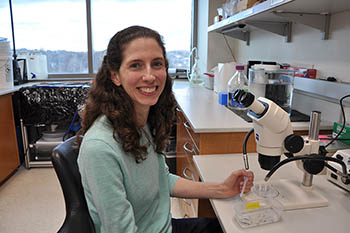 Erin Davies sitting at a microscope and smiling for the camera.