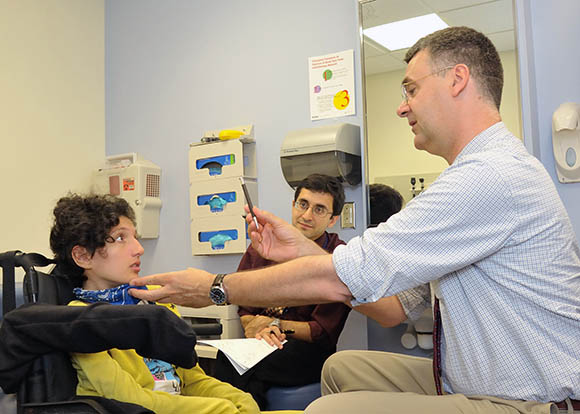 three people in a hospital treatment room; girl is sitting