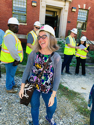 Informal photograph of Sarah Leavitt with hardhat on and several other construction workers with hardhats in front of a building