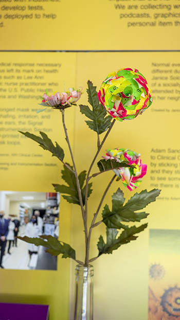 flower constructed from many green, pink, yellow, and red covid screening tags