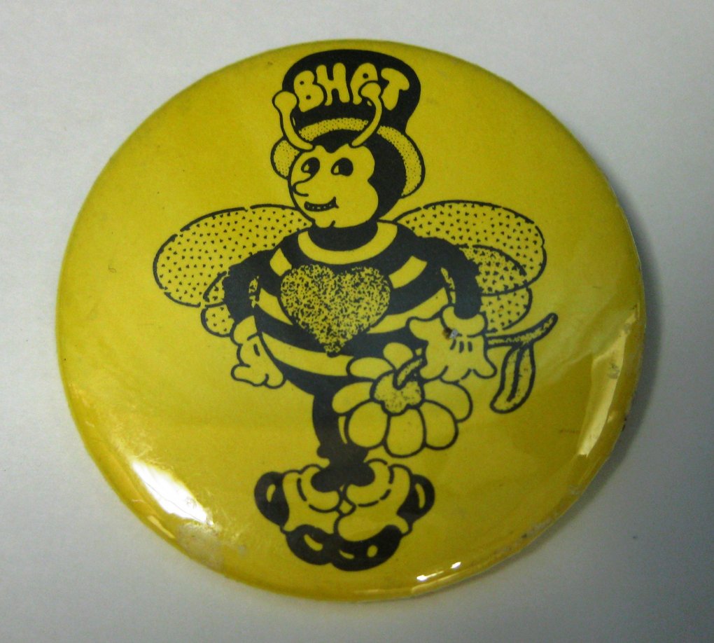 Yellow pin with illustration of a bee holding a flower and wearing a top-hat with the word “BHAT”