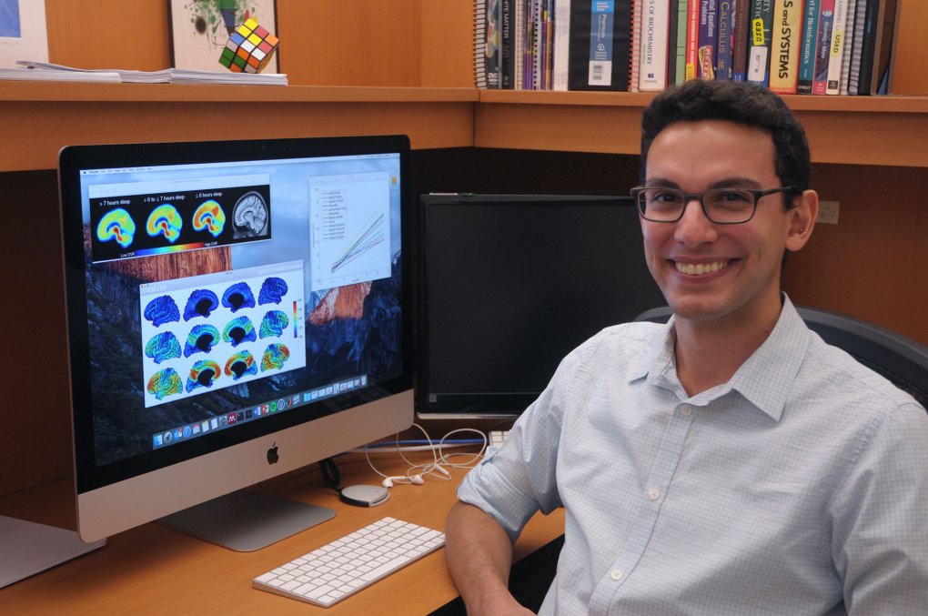 Murat Bilgel, NIH IRP postdoc, at his desk with brain scans