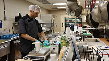man with hairnet preparing food in a commercial-type kitchen