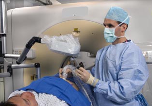 Brad Wood at an imaging machine with patient. Wood is wearing a surgical mask.
