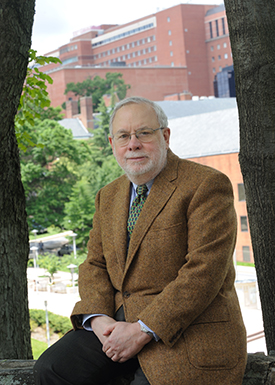 Alan Schechter sitting on a stone wall with Clinical Center in background