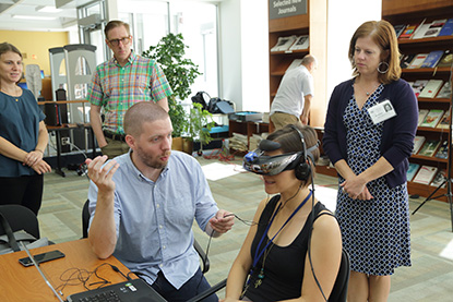Several people watching a woman who's wearing virtual reality headgear.