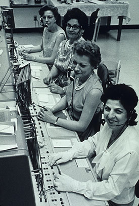  three women wearing headsets and sitting at a switchboard