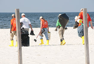 five men, wearing yellow boots, carrying rakes and other clean-up equipment on the beach