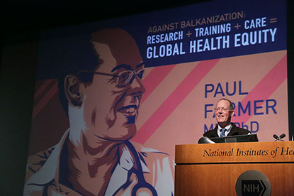 Paul Farmer with a huge illustration of himself on the screen behind him.
