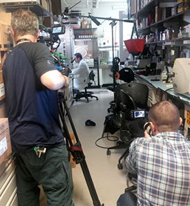 Two cameramen filming a researcher in the lab.