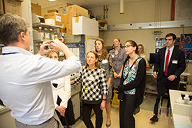 Several people visiting a lab watching a demo by a scientist.