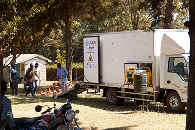 Truck and building with three men walking toward truck and one coming down the stairs from the truck.