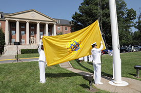 two people in white uniforms raising a yellow Public Health Service Flag