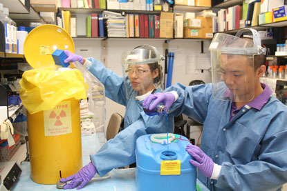 two people in lab wearing protective gear and disposing of radioactive waste