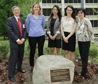 group of five people standing behind a stone with a plaque on it