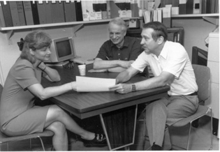 Three people sitting at a table in a conference room.