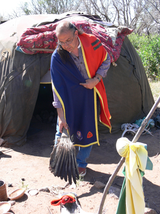  man in Native American attire in front of a sweet lodge