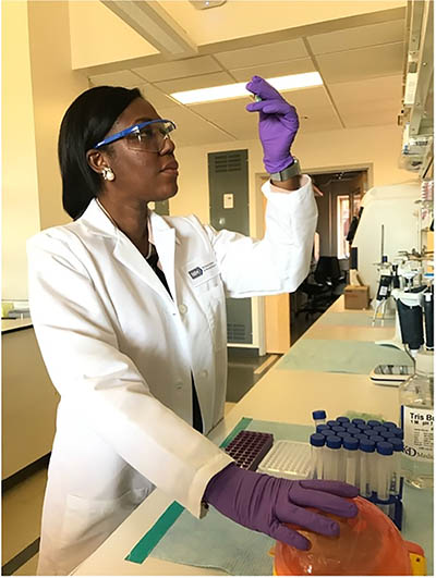 Black woman scientist holding up test tube and looking at it.