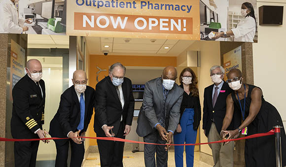 people leaning over a ribbon stretched across opening of new pharmacy