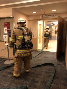 two firemen carrying a hose through a hospital area