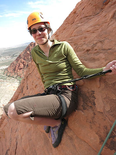 woman in yellow helmet hanging onto a rope on a mountainside