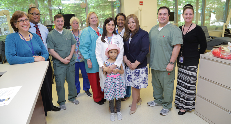 a young girl who received platelets from the NIH Blood Bank poses with staff from the NIH Department of Transfusion Medicine