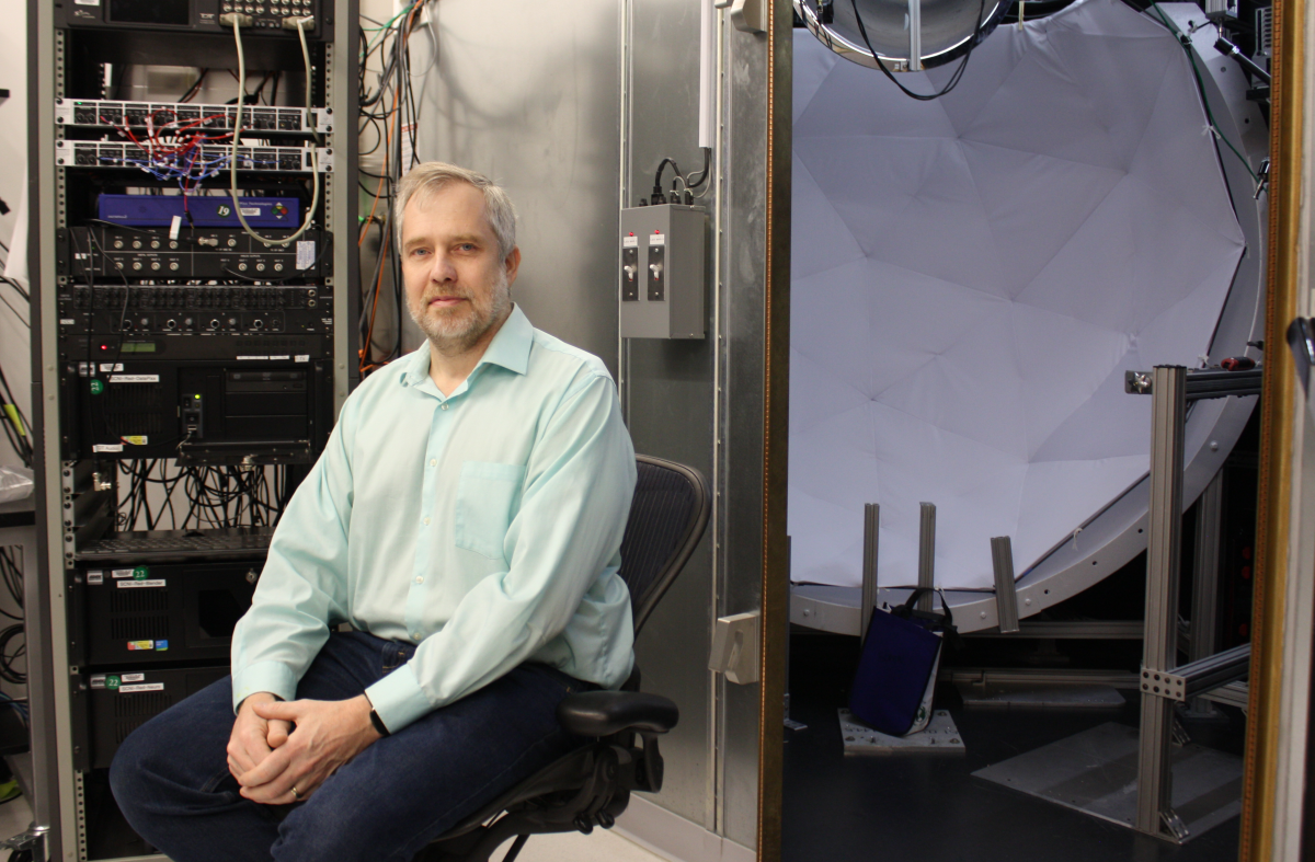 Dr. David Leopold sitting in front of an electrophysiology chamber equipped with a screen and projector.