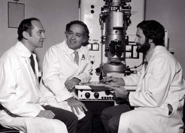 Robert Purcell (left) and Albert Kapikian (center) talking next to a laboratory microscope