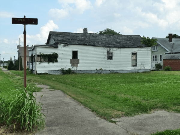 house in poor condition next to an overgrown sidewalk