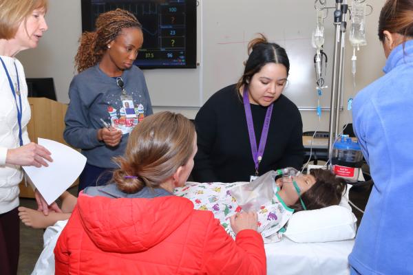 Julie Hogan, a simulation champion, guides participants in conducting a comprehensive neuro-assessment on Diana Tobin, a simulated pediatric patient (PediHAL S2225) with a medical history of Batten disease in status epilepticus.