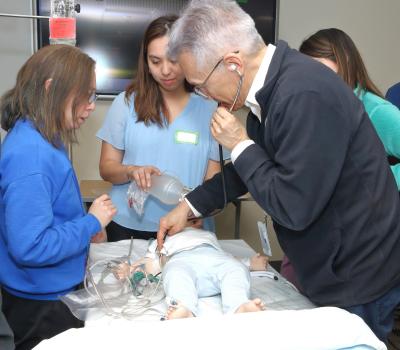 Thomas Burklow (right), director of the simulation program, shows a group of participants how to conduct a rapid assessment on Diego Sanguinetti, a simulated pediatric patient (SimBaby) with a medical history of GM1 gangliosidosis and a cardiac arrhythmia, during the “Pediatric Bridge to Practice” course in February 2025.